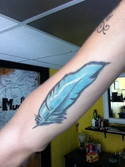 Pluma azul tatuada en brazo